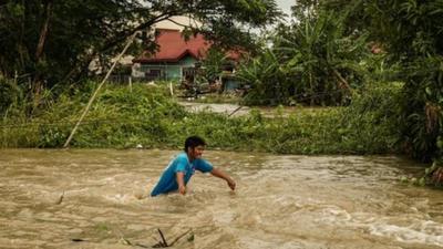 A man struggles to walk down a road which is waist high in water.