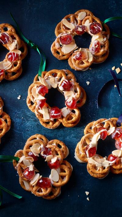 Top down view of pretzel wreaths topped with cherries and almonds on a blue cloth