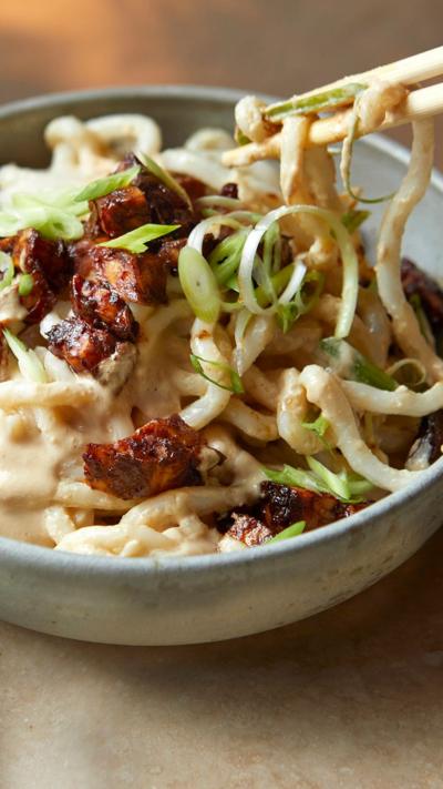 A pair of chopsticks takes some udon noodles out of a bowl.