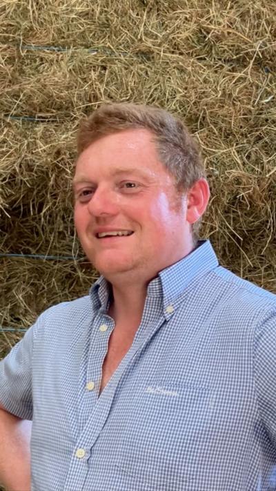 Man in blue and white checked shirt in fron of bales of hay