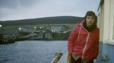 Arena reporter, wearing a red coat, travels on a boat