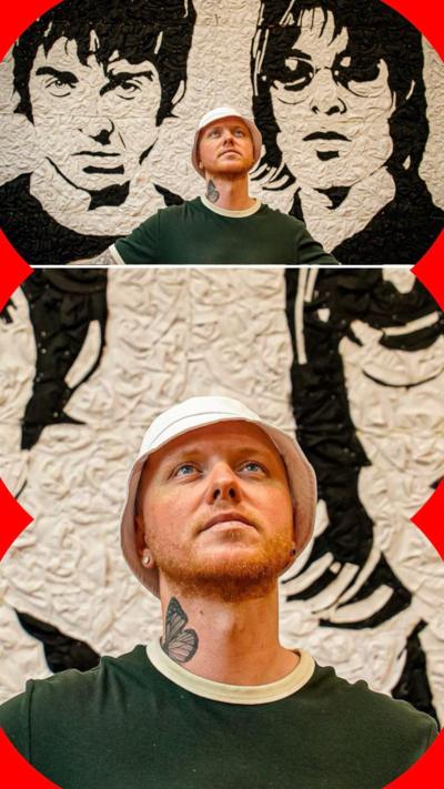A man wearing a bucket head looks up. Behind him is an artwork for Noel Gallagher and Liam Gallagher 