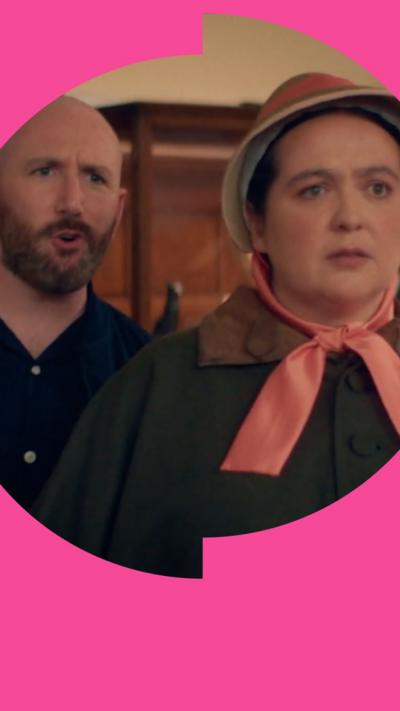 A woman in a bonnet looks away as a bald man with a beard talks behind her.