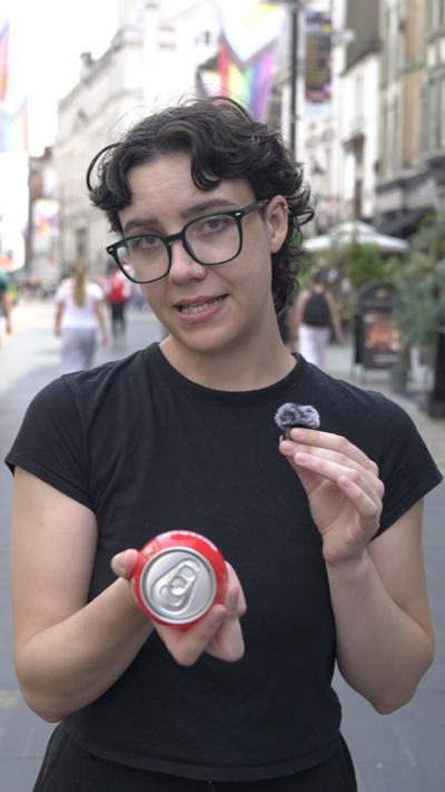 A woman with dark hair, wearing glasses and a black t shirt, holding a red drink