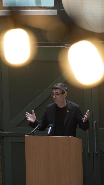 Burnham speaking at lectern during event, has both his hands raised