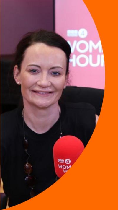 Dr Helen Wall smiles at the camera. She sits in-front of a red BBC Woman's Hour mic.