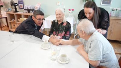 Andy Burnham in care home holding an elderly man's hand.