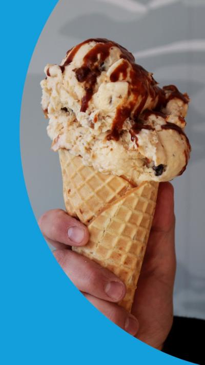 A hand holding a waffle cone of pale colour ice cream covered in sauce.