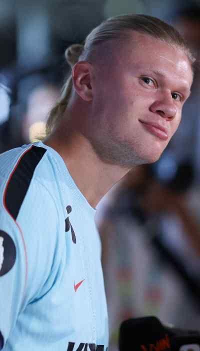 Footballer Erling Haaland looks at the camera. He is wearing a light blue football training top with black markings. He has long blonde hair tied back