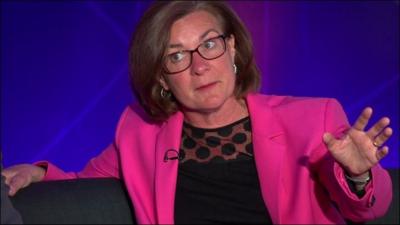 Eluned Morgan wearing a black top and pink jacket, talking with arm outstretched