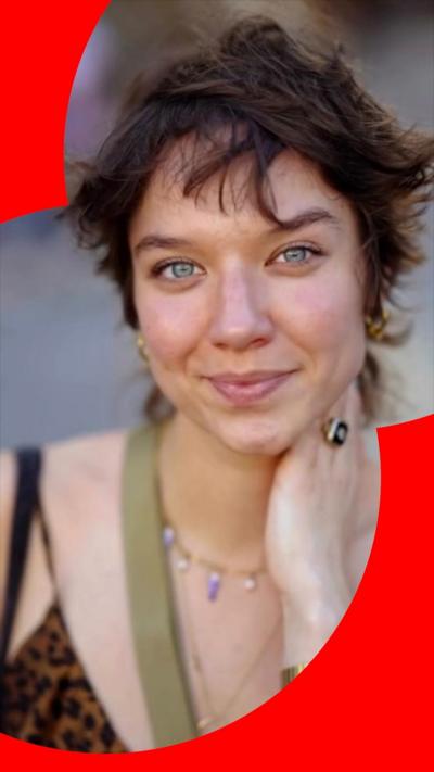A medium close-up portrait of a woman short, dark brown hair. She is smiling with her mouth closed and looking directly toward the camera. She is wearing a black top with leopard print pattern.
