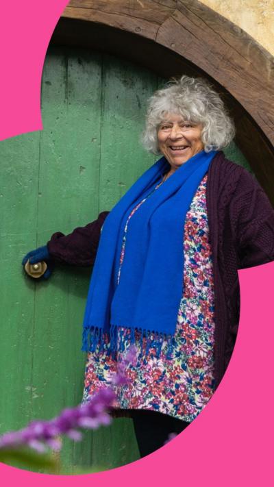 Miriam Margolyes stands outside the circular green door of a Hobbit house