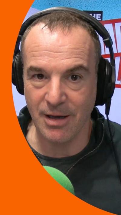 A man, Martin Lewis, wears a dark green jumper and headphones. He's sitting in a radio studio.
