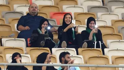 Veiled girls use their phones in a football stadium