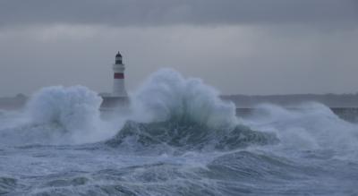 A lighthouse with crashing waves in stormy weather. 