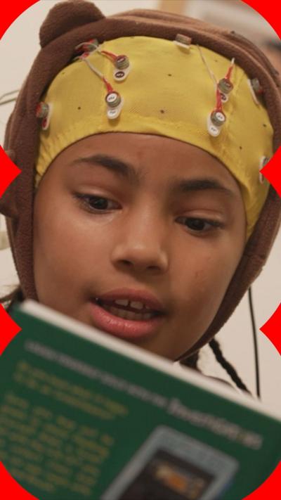A child wearing a brain monitor cap with wires and nodes, reading a book