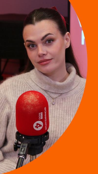 Charli sits in front of a microphone. She wears a beige jumper, her dark hair is pulled back from her face