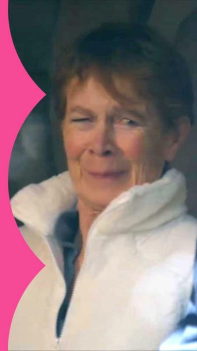 Celia Imrie, suppressing a laugh, wearing a white gilet.