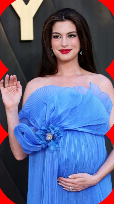 Anne Hathaway waves while placing her other hand on her stomach