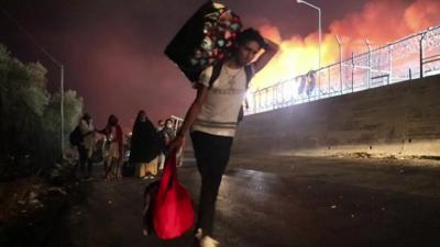 Man carrying bags with fire in the background