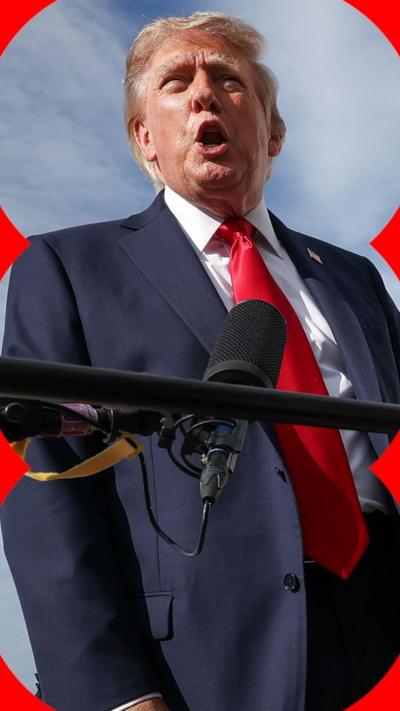 US President Donald Trump, a blond man wearing a navy suit with a red tie, speaks into a microphone.