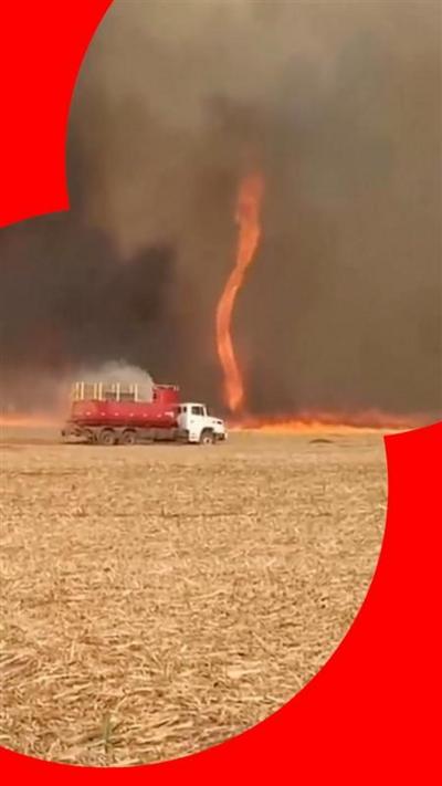 Flames in the shape of a tornado on a field, with a truck spraying water on it