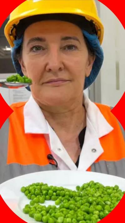 Michelle is wearing a high vis jacket, a yellow hard hat, and holding a plate of peas and a spoon
