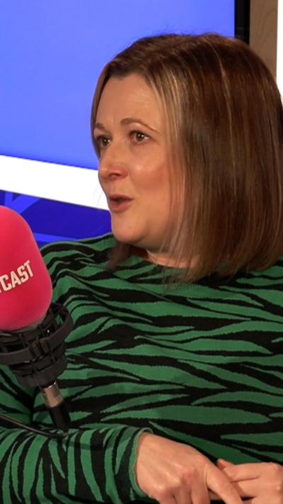 Carole Erskine wears a green and black stripy dress, she is speaking into a red Scotcast microphone