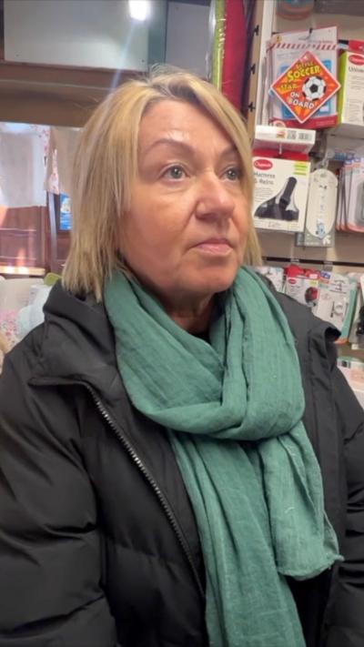 A woman in a green scarf and black jacket stands in a market.