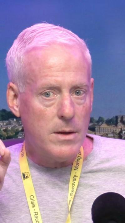 Man with white hair wearing a light top with a yellow lanyard aroung his neck