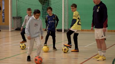 Children watch as a child practices her football skills