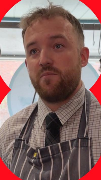 Person wearing a striped apron, checked shirt and tie indoors.