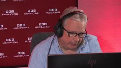 Dòmhnall Moireasdan a' leughadh nan naidheachdan an stiùidio rèidio