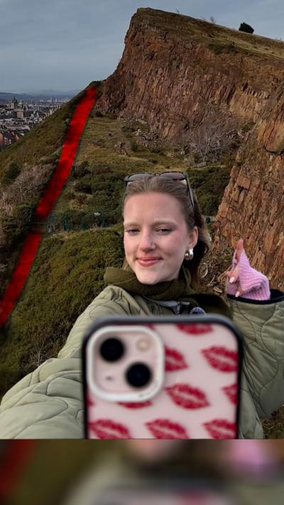 Girl holding iphone with red kisses patterned on it. She is pointing to a section of Arthurs seat, which is in the background.
