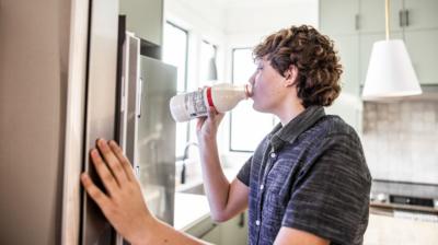 A young man stands by a fridge, drinking milk straight from the bottle