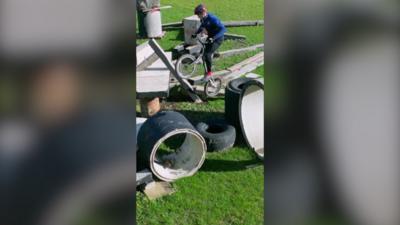 Charlie rides his bike on an obstacle course made up of multiple objects on grass