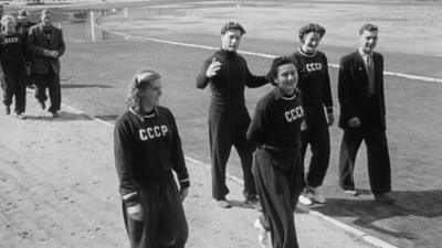 Young people in tracksuits walk around an athletics track