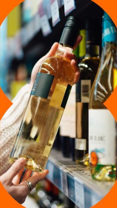 The hands of a woman holding up a bottle of wine in the isle of a shop