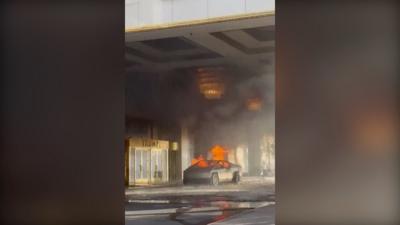 A Tesla truck has large flames emerging from it outside a golden doorway with "TRUMP" emblazoned above it.