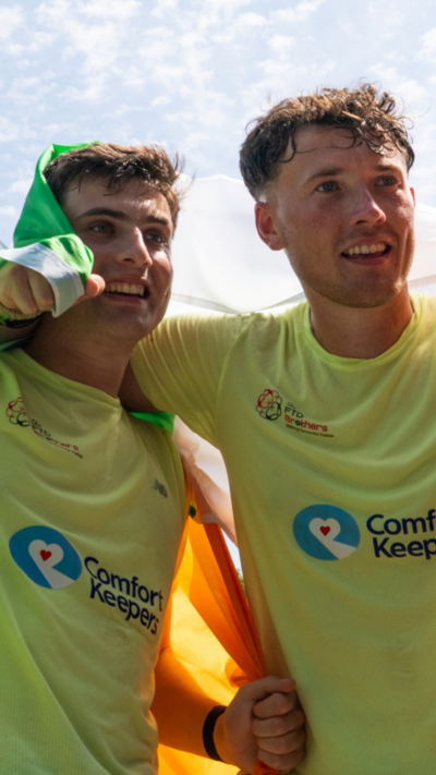 Cian and Jordan Adams have their arms around each other and are holding an Irish tricolour above their heads as they celebrate finishing their 33 marathons in 33 days challenge.