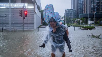 Man carries woman on his back in flooded street