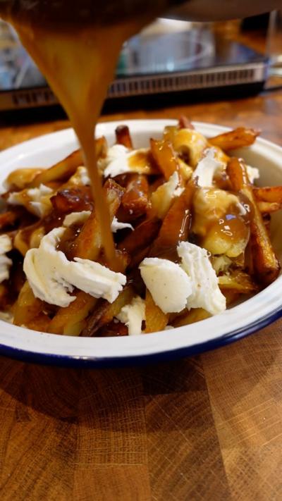 An enamel plat of chips with cheese and gravy being poured over