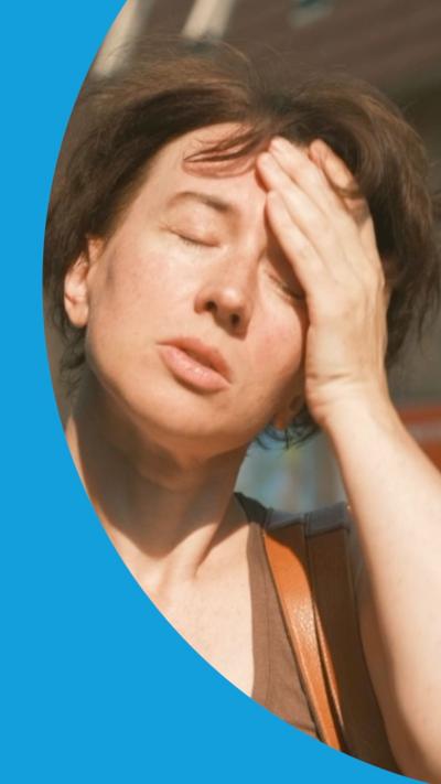 A woman in direct sun holds her left hand to her head and closes her eyes.