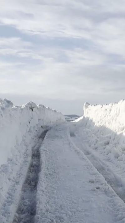 A snow with stacks of snow to either side from the point of view of someone in a car
