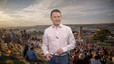 Matt standing in front of a picture of people on Glastonbury field