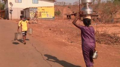 A man and a woman carry water up a dust road.