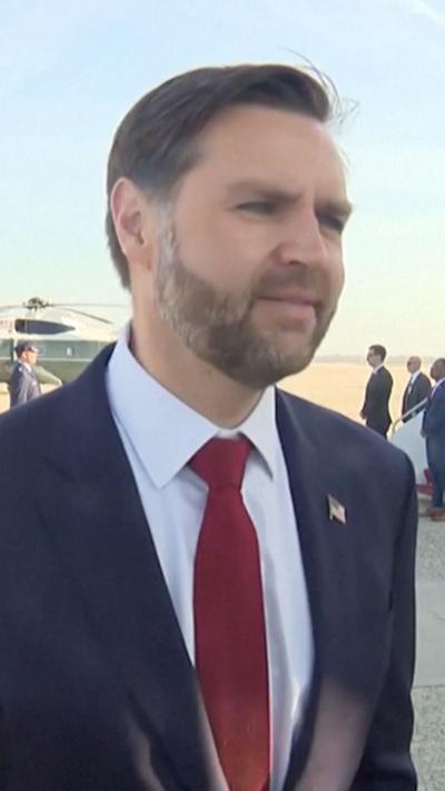 JD Vance is photographed from below wearing a blue suit, white shirt and red tie. 