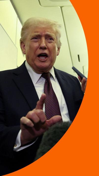 Donald Trump wears a suit and tie and talks with his hand raised