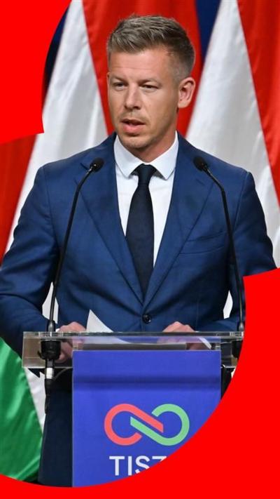 Peter Magyar holds a press conference in Budapest. He wears a blue suit and stands against a backdrop of the Hungarian flag.