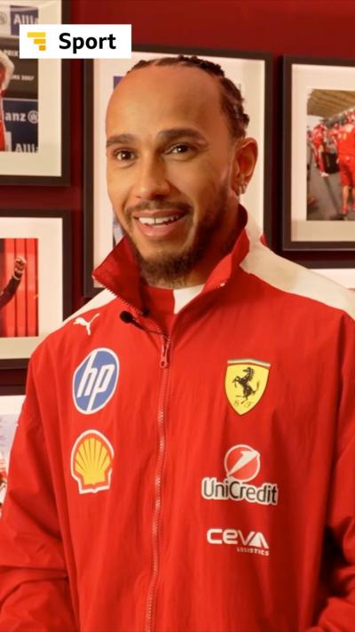 F1 driver Lewis Hamilton smiles. He is wearing a red Ferrari jacket